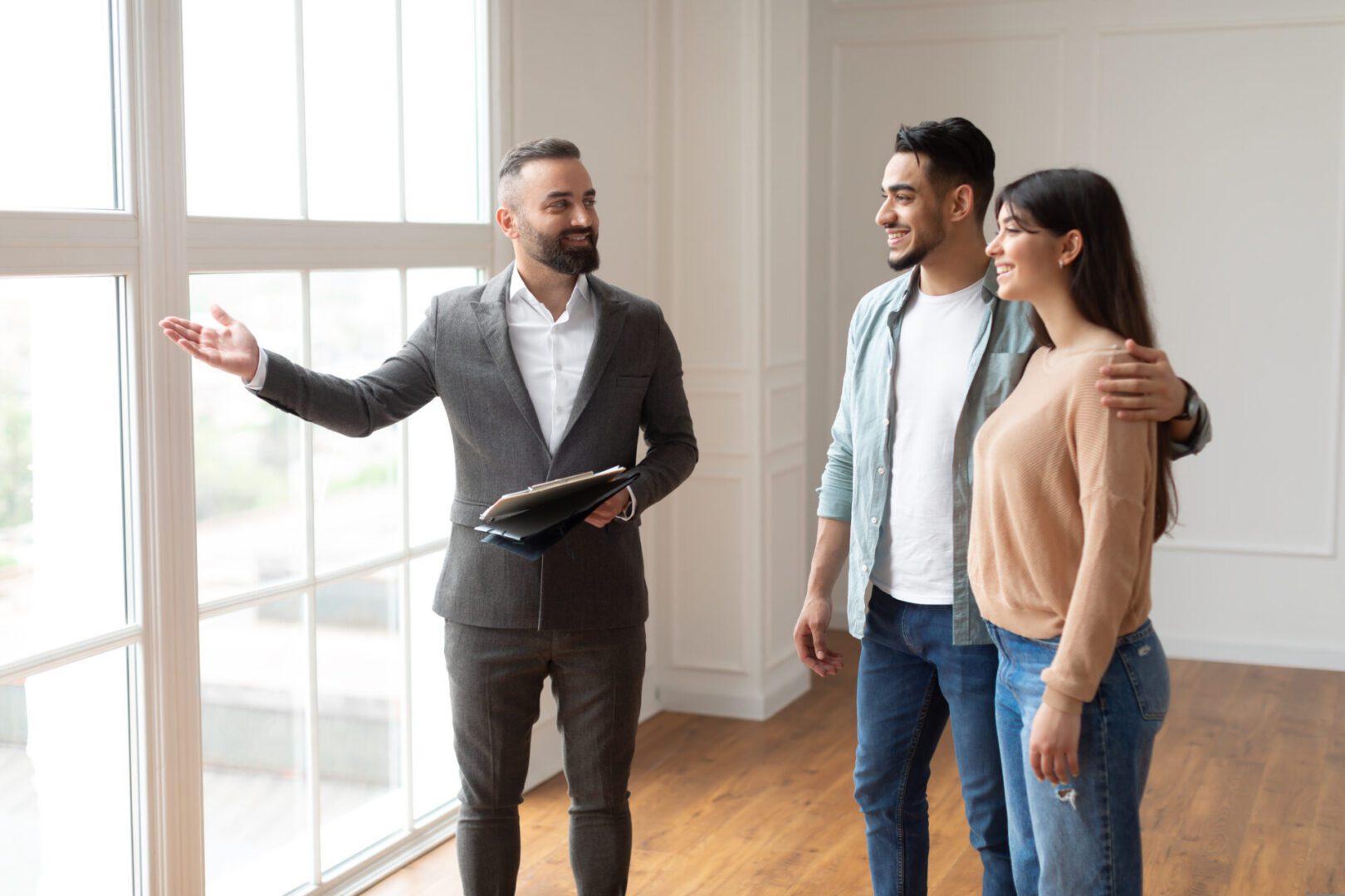 Estate Agent In Suit Showing Buyers New Apartment Real estate agent showing couple a house.